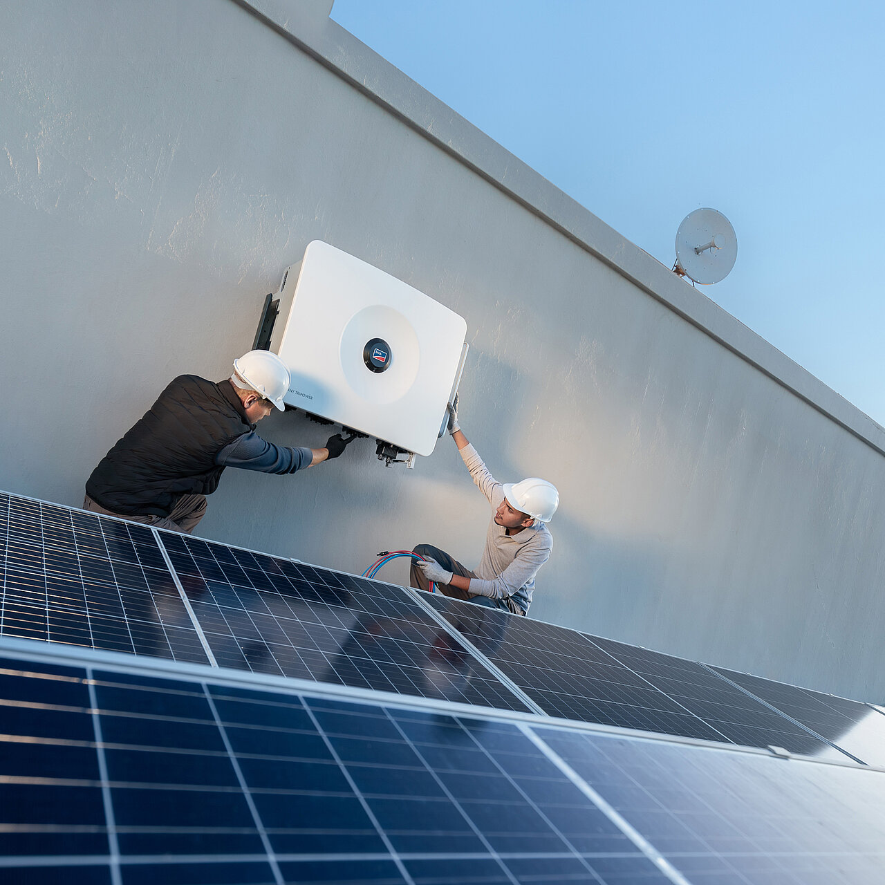 Zwei Installateure montieren einen Sunny Tripower 125 für eine Gewerbeanlage mit Solarmodulen