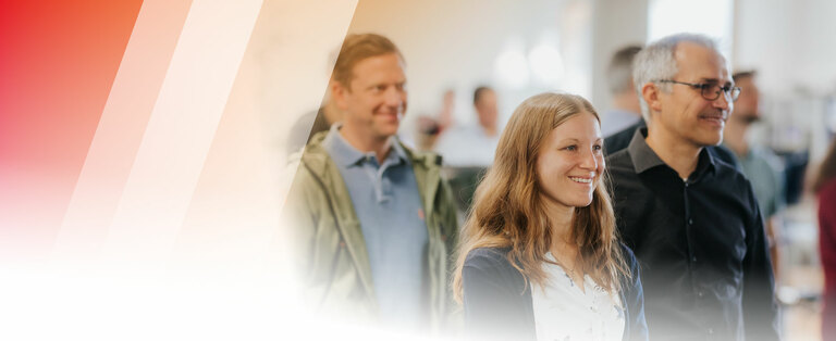 Mehrere Personen sind zu erkennen. Fokus liegt auf einer Frau, die lächelnd an der Kamera vorbeischaut. 