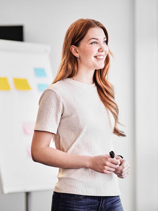 Eine junge Frau steht lächelnd vor einem Fenster und sieht nach draußen. 