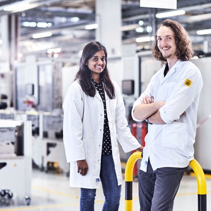 Zwei Personen, eine Frau und ein Mann, stehen in ESD-Kitteln in der Produktion. 