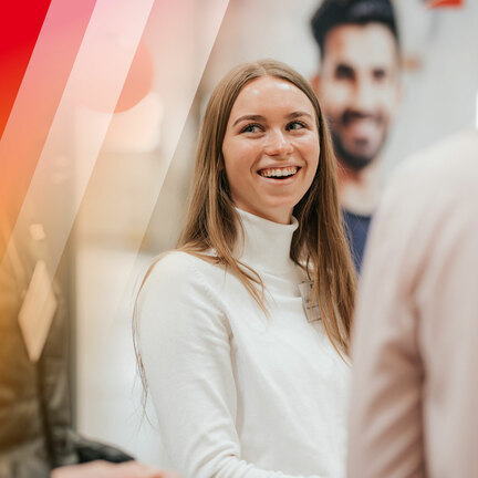 Eine Frau mit weißem Pullover steht im Fokus und lacht.