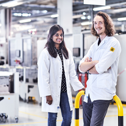 Zwei Personen, eine Frau und ein Mann, stehen in ESD-Kitteln in der Produktion. 