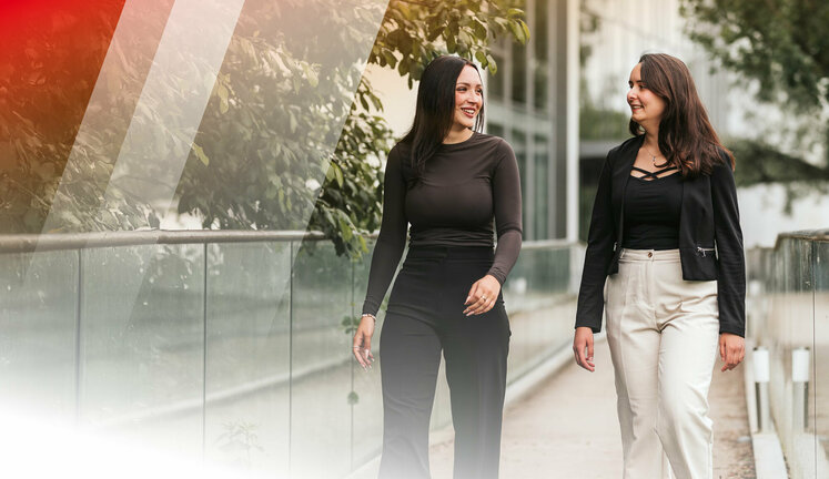 Zwei junge Frauen laufen im Freien und schauen sich lachend an. 