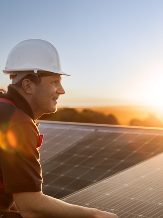 Ein Techniker steht vor einem Solarpanel und schaut in den Sonnenuntergang. 