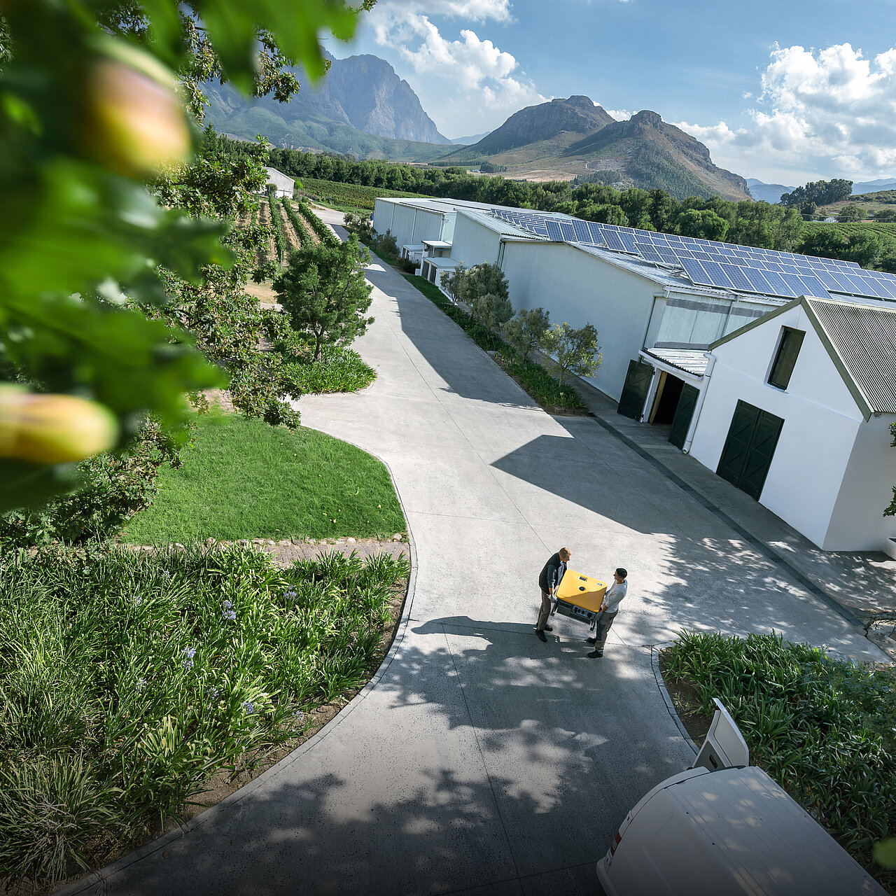 Lagerhallen mit einer PV-Anlage auf dem Dach, davor tragen zwei Installateure einen Sunny Island X