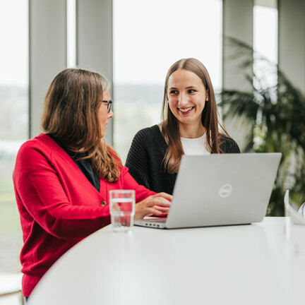 Eine ältere Frau zeigt einer jüngeren Frau etwas auf einem Laptop.