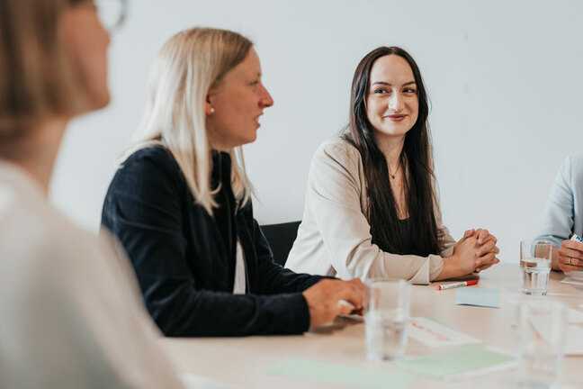 Mehrere Personen sitzen an einem Tisch, zwei Frauen sind im Fokus. 